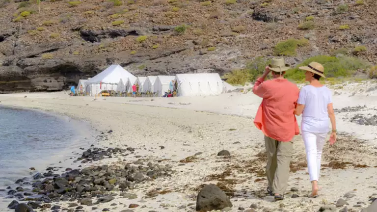 A couple walks along the beach with Camp Cecil de la Isla in the distance, on Espiritu Santo, part of a UNESCO World Heritage Site in Baja, Mexico