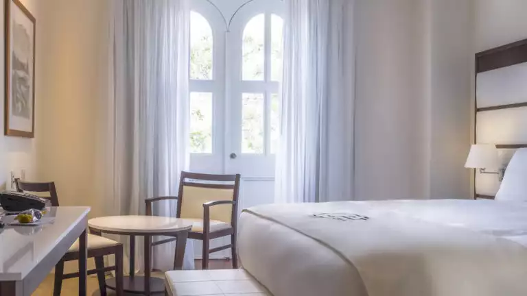 Large windows allowing bright natural light in a Premium Suite with large bed, small table and chairs at Central Hotel Panama in Panama City