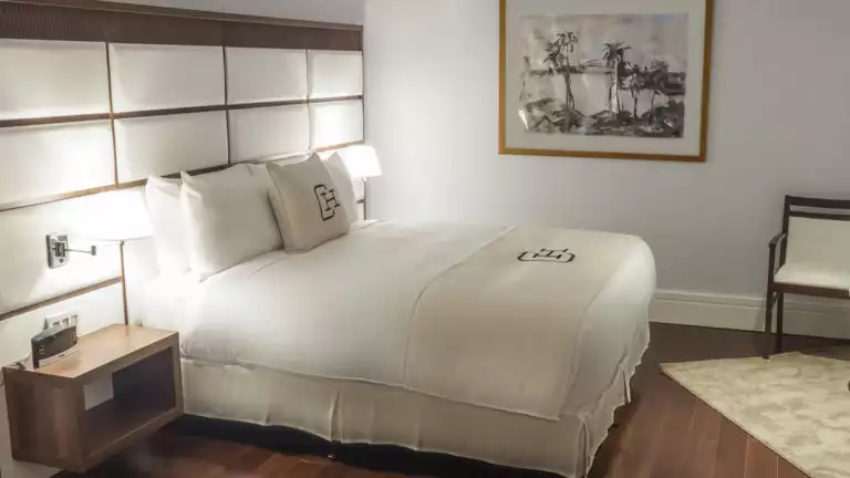 Painting of ocean coast and palm trees adorning wall near large bed in a suite at Central Hotel Panama in Panama City