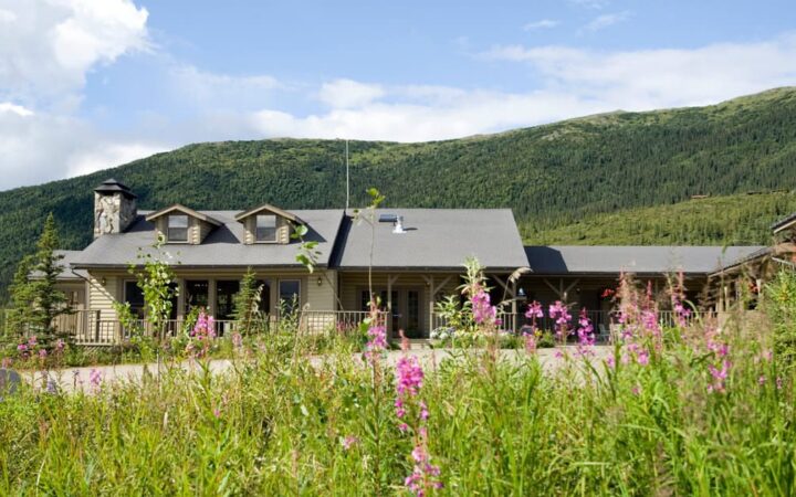 The North Face Lodge, set in the Alaskan wilderness next to a field of wildflowers and hills, is a traditional north-country inn located within Denali National Park