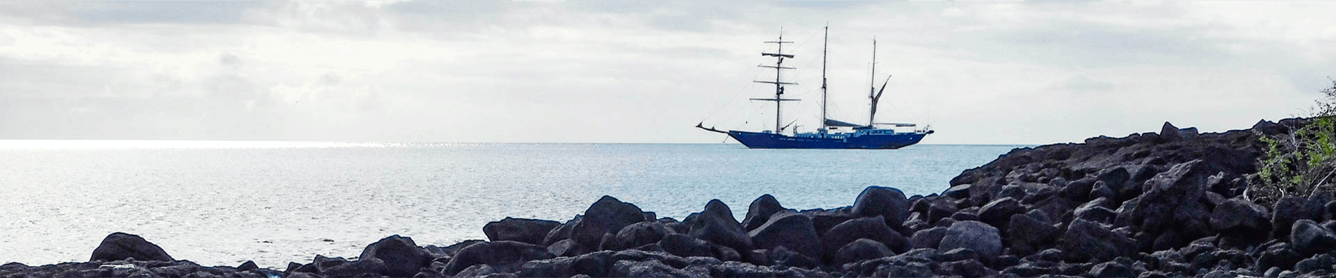galapagos small ship anchored at sea on a calm overcast day with rocks in the foreground