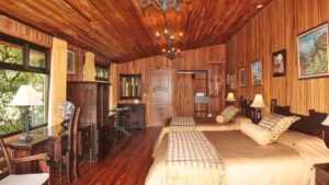 Suite interior with two beds, desk, table and chairs, dresser and wood finishings at Hotel Fonda Vela in Monteverde, Costa Rica