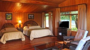 Interior of Standard Room with two beds, table and chairs, TV and windows at Hotel Fonda Vela in Monteverde, Costa Rica
