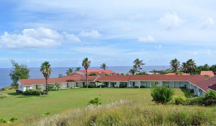 exterior view of hotel iorana easter island in chile with a large lawn around it, sunny skies above and the ocean in the distance