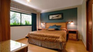 room with king bed with gold quilt, blue wall and picture above it and window on the left at hotel ladera in panama