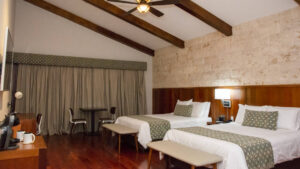 A guest room with two twin beds, wooden beams, a ceiling fan, drapes, and a television at the family-owned Los Brezos Hotel, near the Baru Volcano in Panama