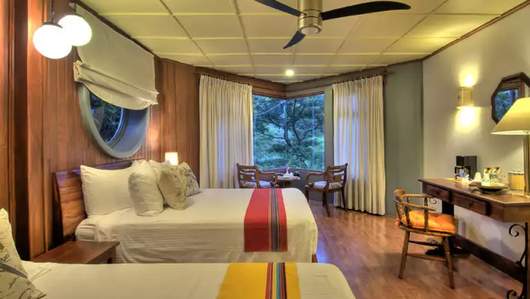 Two twin beds and a desk with a private balcony overlooking the jungle at the Monteverde Lodge, a sustainable, nature retreat on the edge of a well-known cloud forest in Costa Rica