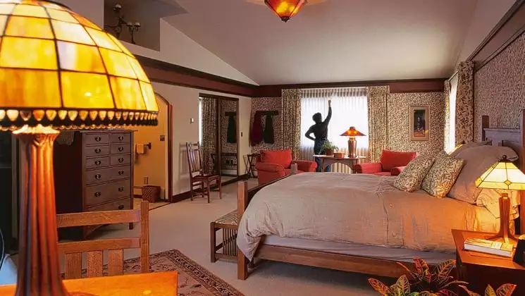 A woman draws the curtains inside a guest room with a large bed and reading lamp at the Parkside Guest House, a bed and breakfast in Anchorage Alaska