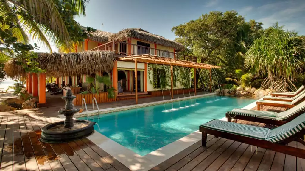 The pool with lounge chairs and umbrellas at the Inn at Robert's Grove, a boutique hotel ideal after a day exploring Belize's barrier reef or tropical rainforest