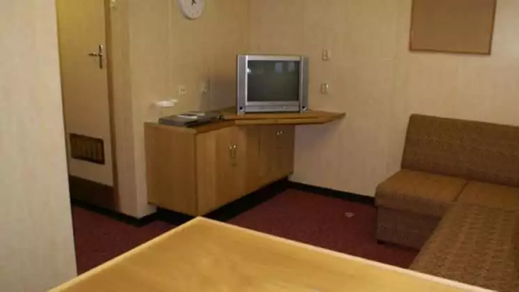 50 Years of Victory mini suite seating area, an L shaped couch with table and TV, with bed, closet, and night stand.