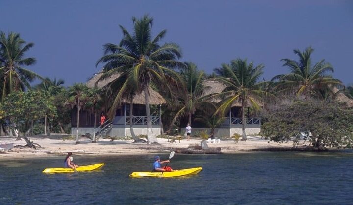 Two kayakers paddle in the ocean, in front of the pristine beach, where the Blackbird Caye Resort in Belize is located