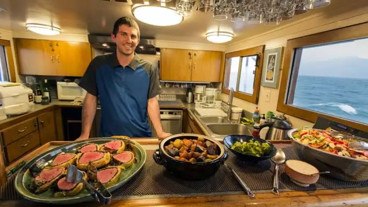 Man in galley with freshly prepared food aboard Discovery classic working yacht in Alaska