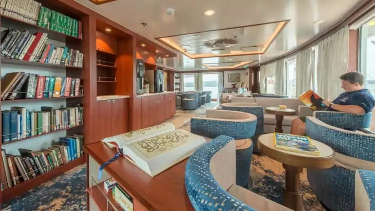 Man reads in armchair beside large window in library aboard National Geographic Endeavour II expedition ship in the Galapagos Islands
