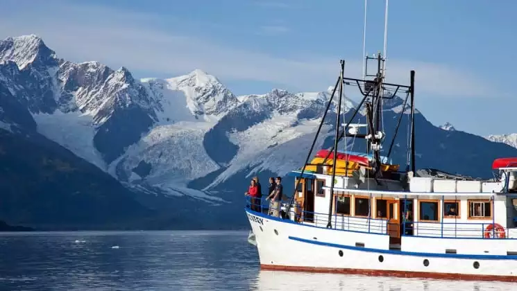 Four people at the port bow aboard Discovery yacht in Alaska, as seen from nearby kayak