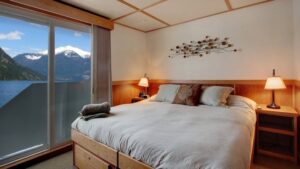 Admiral stateroom with large bed with pillows on it and a large window behind it aboard the Safari Quest pacific northwest small ship