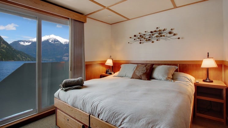Admiral stateroom with large bed with pillows on it and a large window behind it aboard the Safari Quest pacific northwest small ship