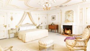 all white room with a large bed, ottomans and fireplace aboard the Sea Cloud mediterranean luxury yacht