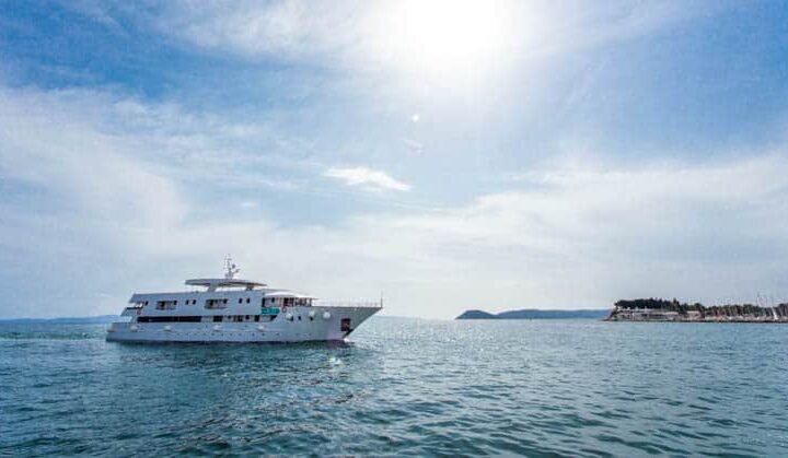 The Adriatic Sun small ship cruising on calm seas in front of an island.