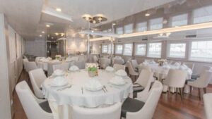 Adriatic Sun small ship dining room with white tables and chairs and many windows.