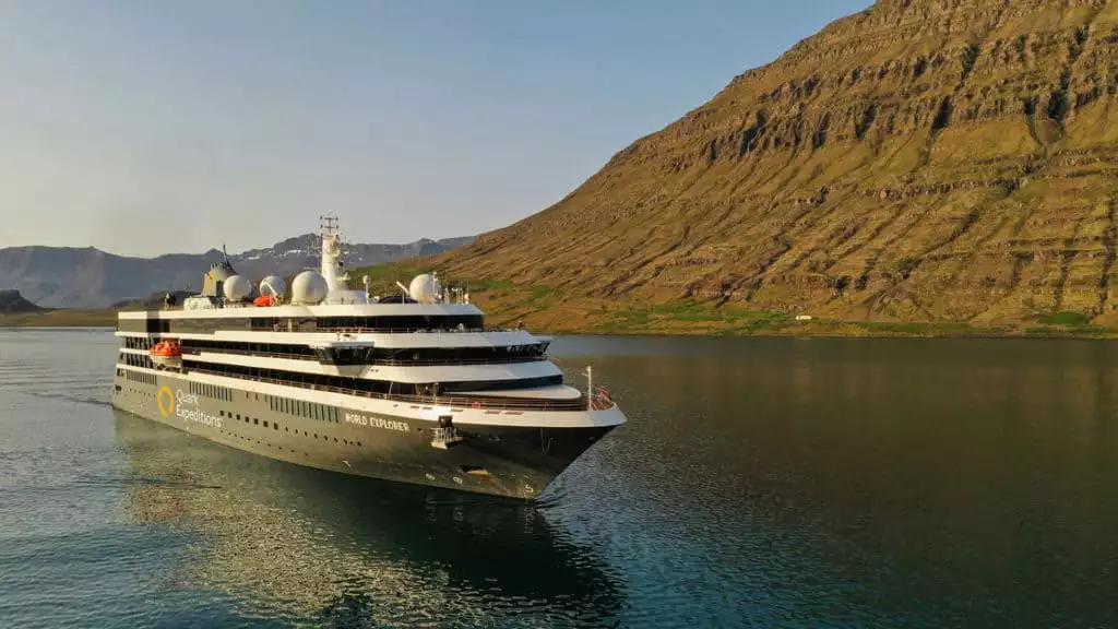 Exterior scenic of polar small ship World Explorer cruising past green and brown hillsides.
