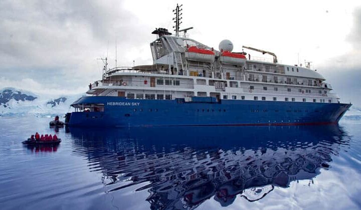 Hebridean Sky Exterior anchored in Antarctica with mountain encased with glaciers and snow.