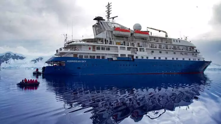 Hebridean Sky Exterior anchored in Antarctica with mountain encased with glaciers and snow.
