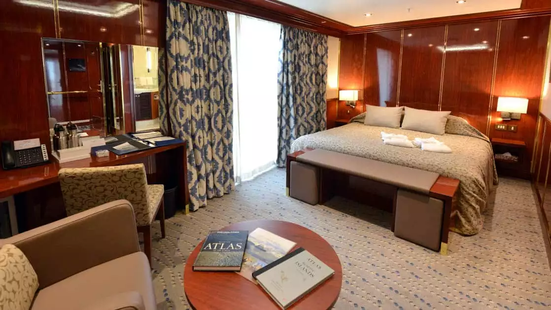 Hebridean Sky Penthouse suite with sliding glass door that leads out to a balcony, queen size bed, cairs and coffee table with a desk.