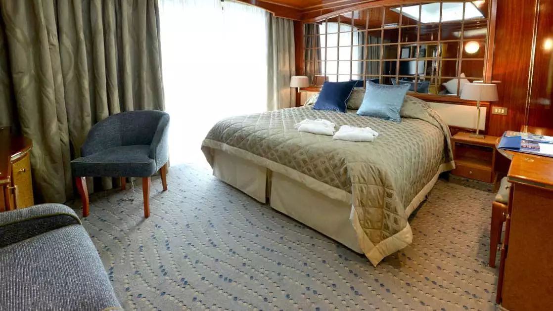 Hebridean Sky Veranda suite with sliding glass door out to the balcony, queen bed, couch and chair, nightstands and desk.