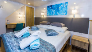 Lower Deck cabin aboard Aquamarin Mediterranean small ship, with double bed, track lighting, wooden bedsie tables & white-&-blue accents.