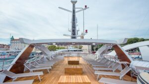 Sun Deck of Aquamarin deluxe Mediterranean yacht, with wooden decking, beige chaise lounge chairs & navigational equipment pole.