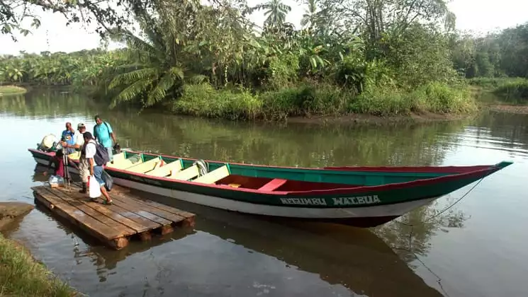a large dugout canoe is tied to a small pier on a river while adventure travelers step out of it to start the best of panama land tour