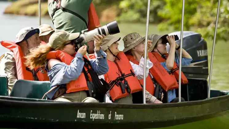 a small skiff boat full of people pointing and taking photographs goes down the river during the best of panama land tour