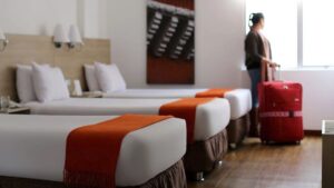 A person stands next to the window inside a traditional room at the Casa Andina Standard Arequipa in Peru with three full beds.