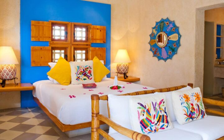 Large bed covered in red flower petals and colorful pillows, with loveseat and Mexican-style artisan wall hangings at Casa Natalia in San Jose del Cabo on the Baja Peninsula