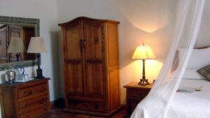 Inside a room, with a mosquito net draped over a queen-sized bed, an armoire, and handcrafted furniture at Todos Santos Inn, an old hacienda hotel in Baja