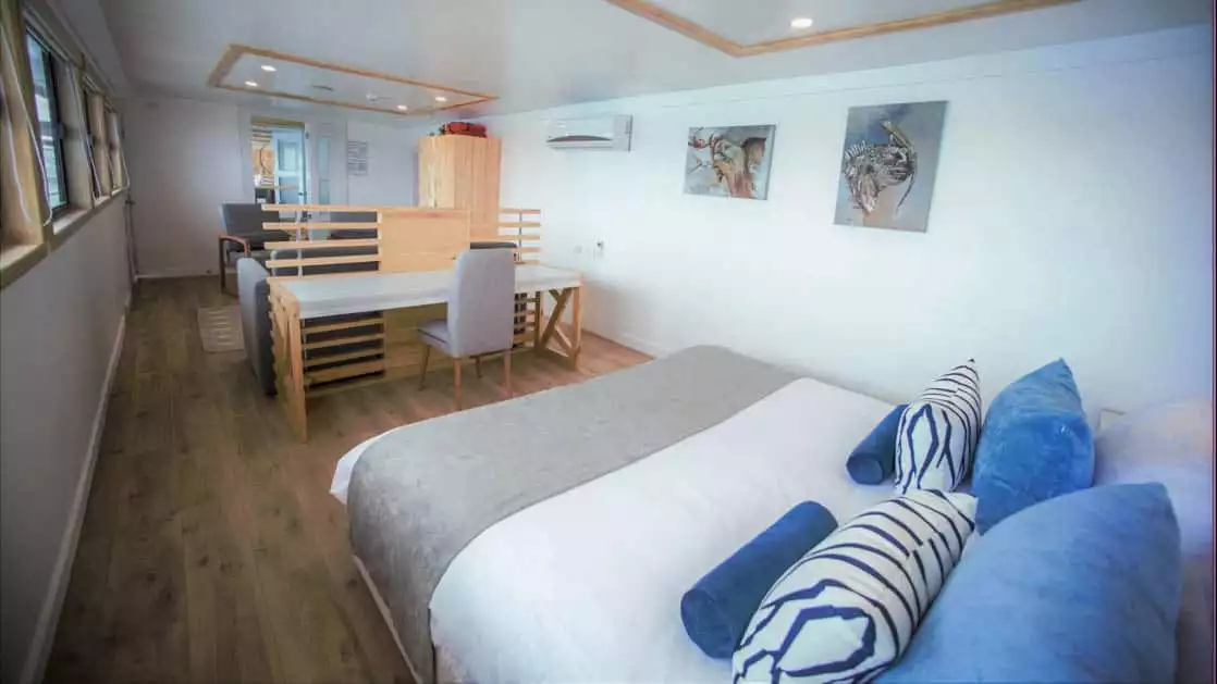 Sea Star Suite aboard the Sea Star Galapagos small ship bed with desk and chair in the background with blue pillows