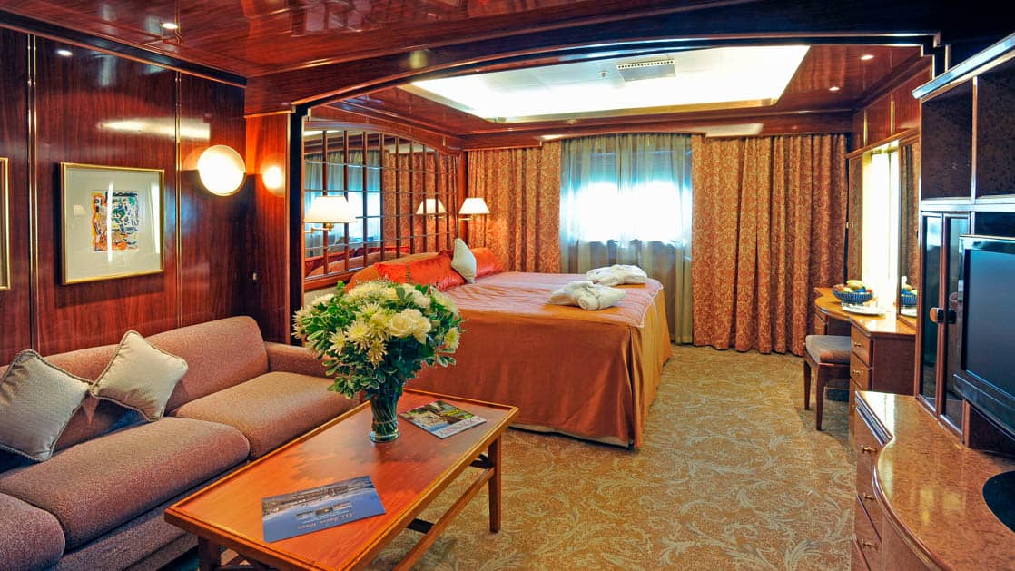 Island Sky Porthole suite with queen bed, porthole and living room with couch, chair and coffee table.