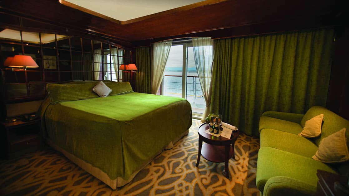 Island Sky Promenade suite with queen bed, couch, nightstands, reading lights and balcony.