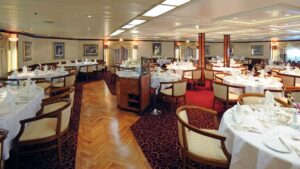 Dining room on the Island Sky with round tables and chairs set for a meal.