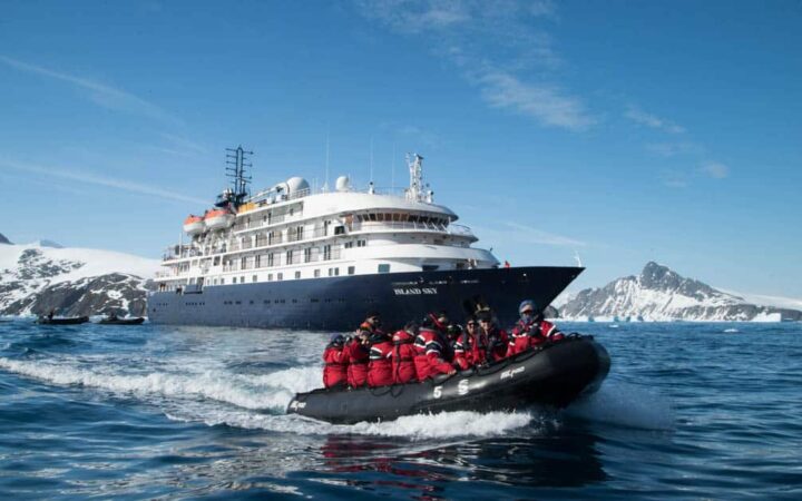 Island Sky anchored off the coast of Antarctica with a zodiac cruising with passengers.