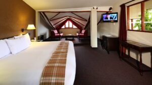 The suite at Casa Andina Classic Cusco San Blas, in Cusco, Peru, features a king-sized bed, wooden beams, a seating area, and a television.