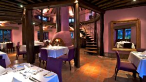 Wooden beams, a brick fireplace, and tables set with white linens for fine dining at the restaurant inside Sol Y Luna, a luxury retreat in the Andes