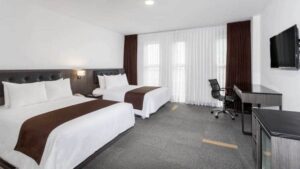 A suite with two queen-size beds, television, dresser, and large windows at the Wyndham Costa del Sol hotel, connected to the Lima International Airport
