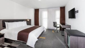 A suite with a king-sized bed, television, dresser, and large windows at the Wyndham Costa del Sol hotel, connected to the Lima International Airport