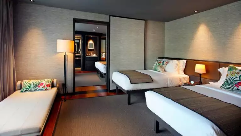 An interconnected suite with an open door between two rooms, a day bed and two double beds with white sheets and tropical pillows.
