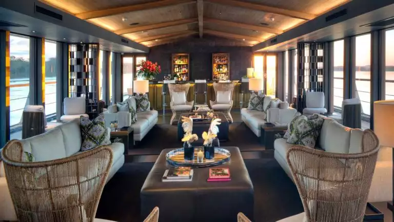 Indoor lounge with long seating area, a bar at the far side, surrounded with floor to ceiling glass windows.