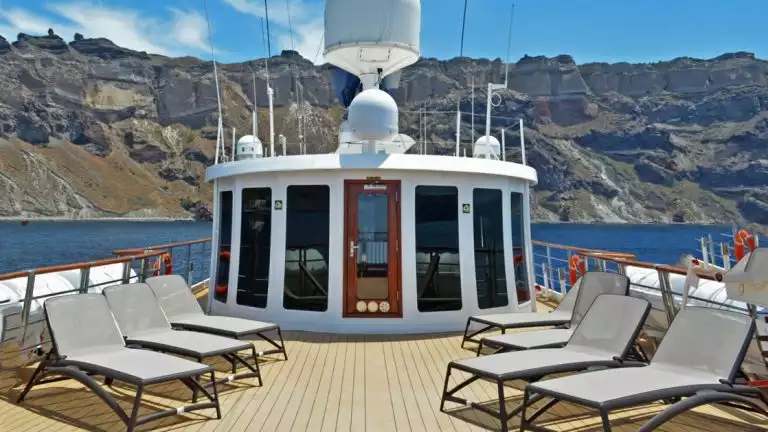 top deck of small cruise ship with lounge chairs in front of rocky landscape and blue waters on a sunny day