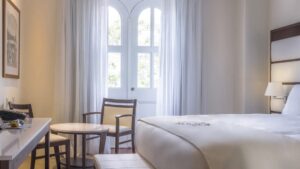 Large windows allowing bright natural light in a Premium Suite with large bed, small table and chairs at Central Hotel Panama in Panama City
