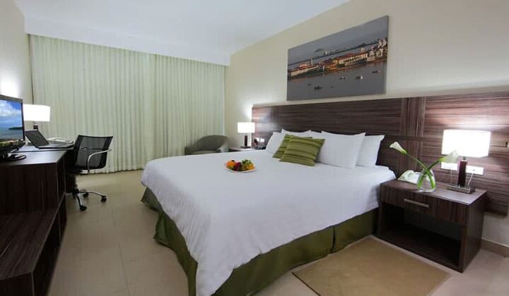 room with a king bed with green accents and a picture on the wall at the clarion victoria panama hotel
