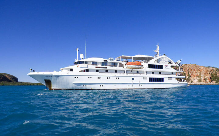 Port side exterior of Coral Adventurer small white expedition ship with 5 decks cruising on a sunny day in Australia.